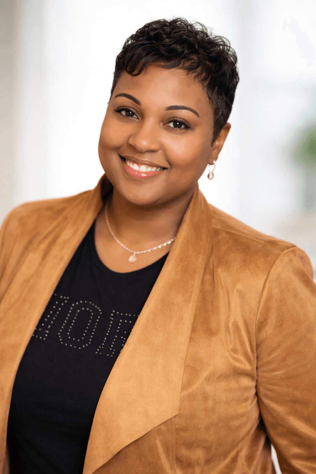 Smiling Black woman with short dark hair wearing a tan blazer and gold necklace.
